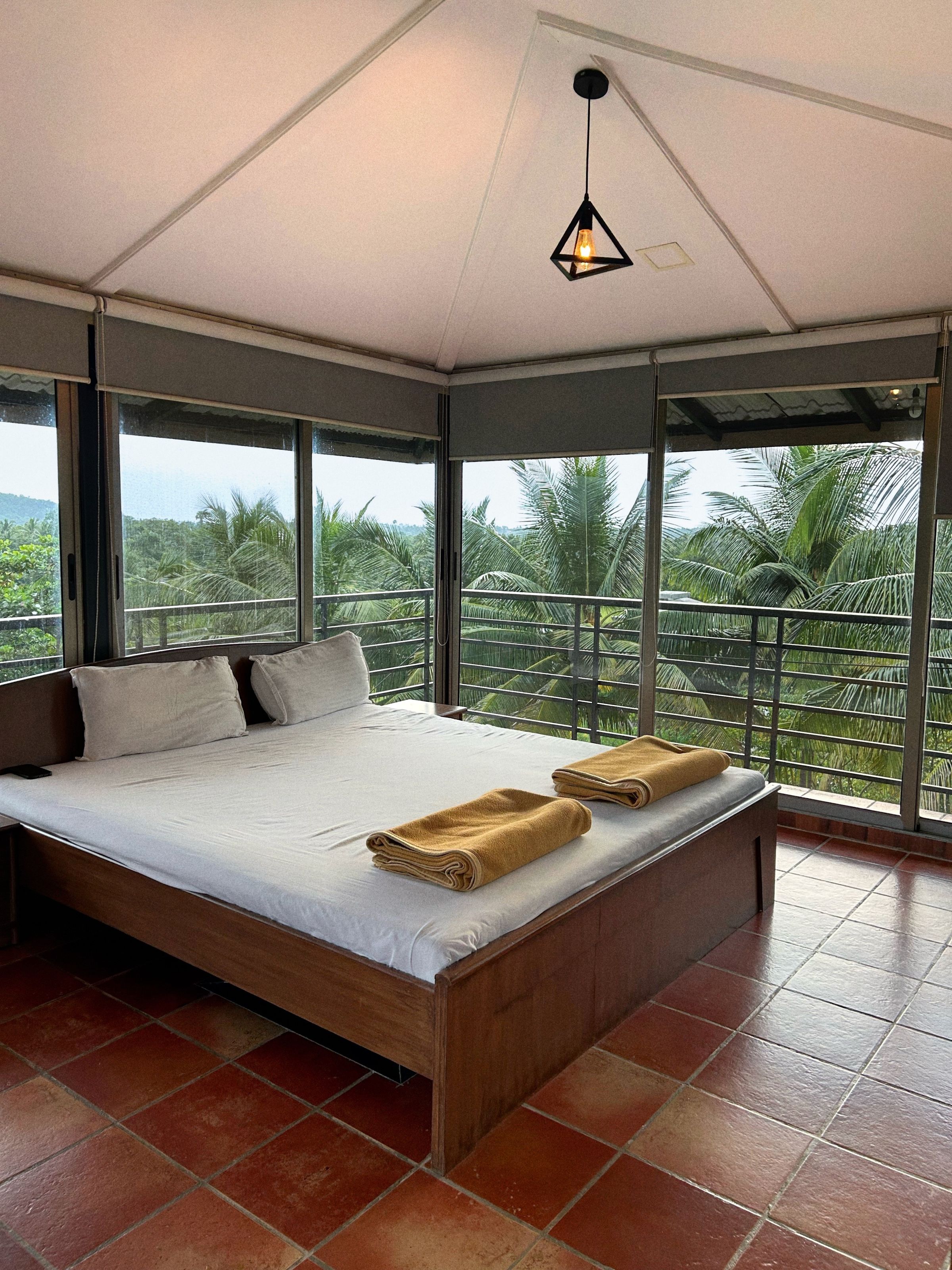 Tropical bedroom with a timber bed, white linen, terracotta floor and tall windows framing dense palm foliage