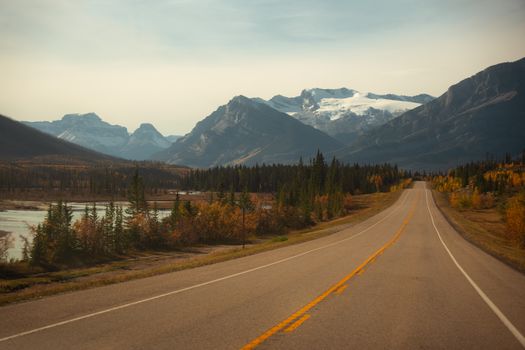 A picturesque road leading to mountains with autumn foliage and a river view.