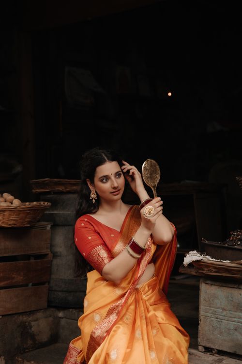 Free Woman in a beautiful saree admiring herself in a mirror, surrounded by rustic decor. Stock Photo