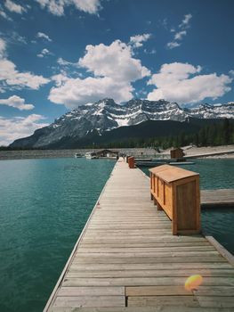 Explore the stunning views of a wooden boardwalk leading to a serene lake surrounded by majestic mountains in Banff, Canada.