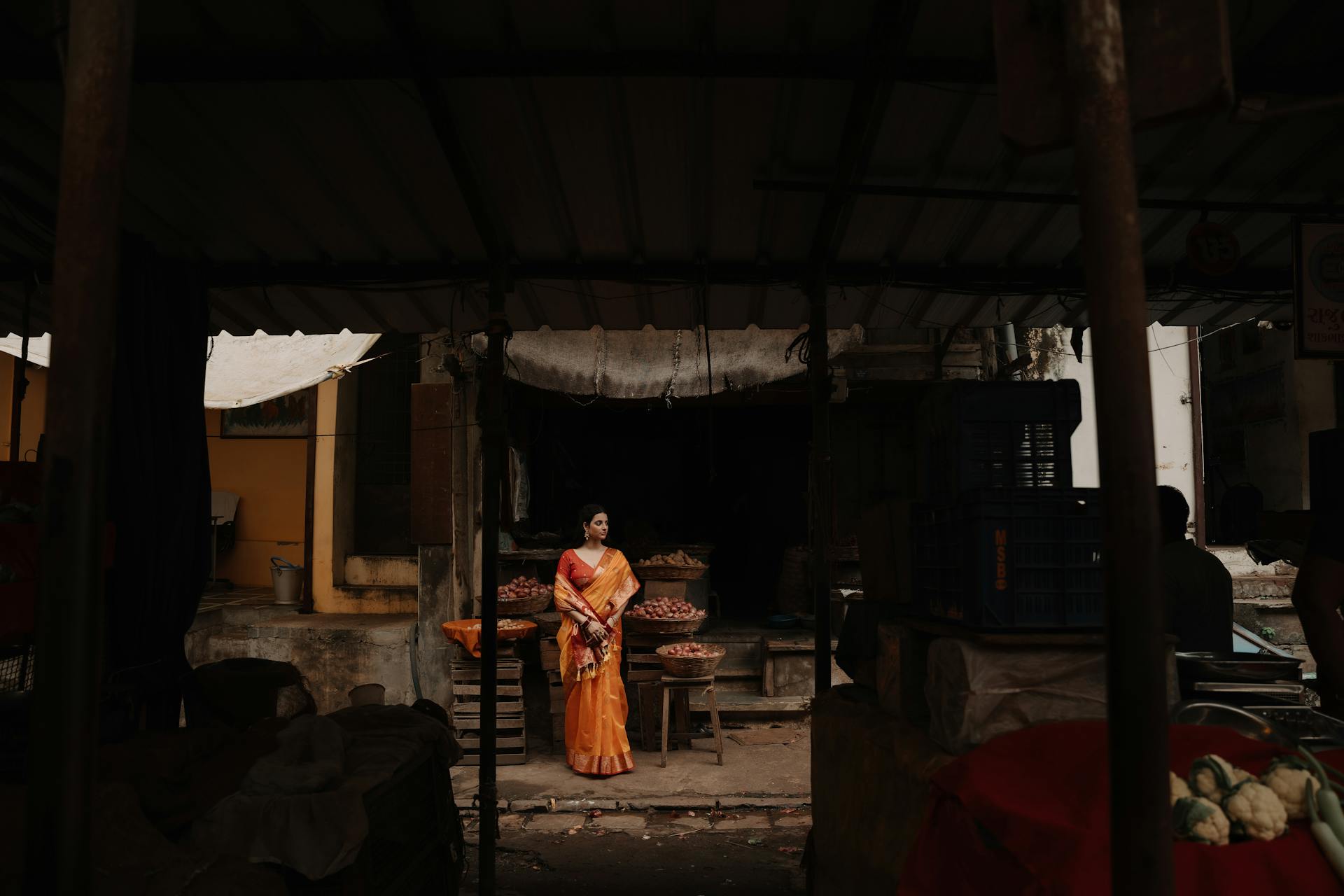 Woman in an orange sari standing in a traditional Indian market stall.