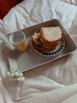 A cozy breakfast in bed setup with sandwiches and a yellow cup on a tray.