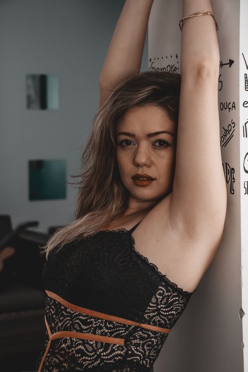 Free Stylish young woman posing with arms raised, leaning against a patterned wall indoors. Stock Photo