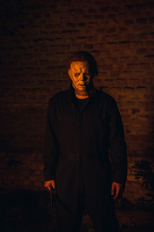 Free Creepy masked figure standing against a brick wall in low light, creating an eerie atmosphere. Stock Photo