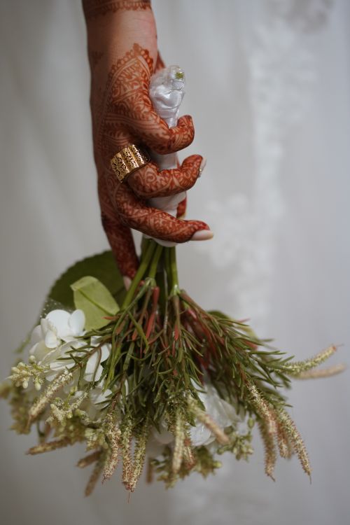 Free A close-up of a hand with henna tattoos holding a bridal bouquet with white flowers. Stock Photo