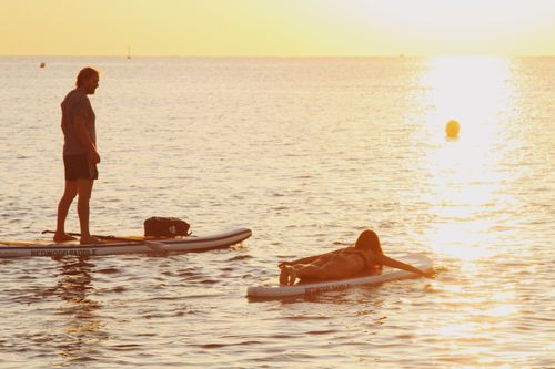 Free Two people enjoying paddleboarding on the ocean during a golden sunset, perfect for leisure and relaxation. Stock Photo
