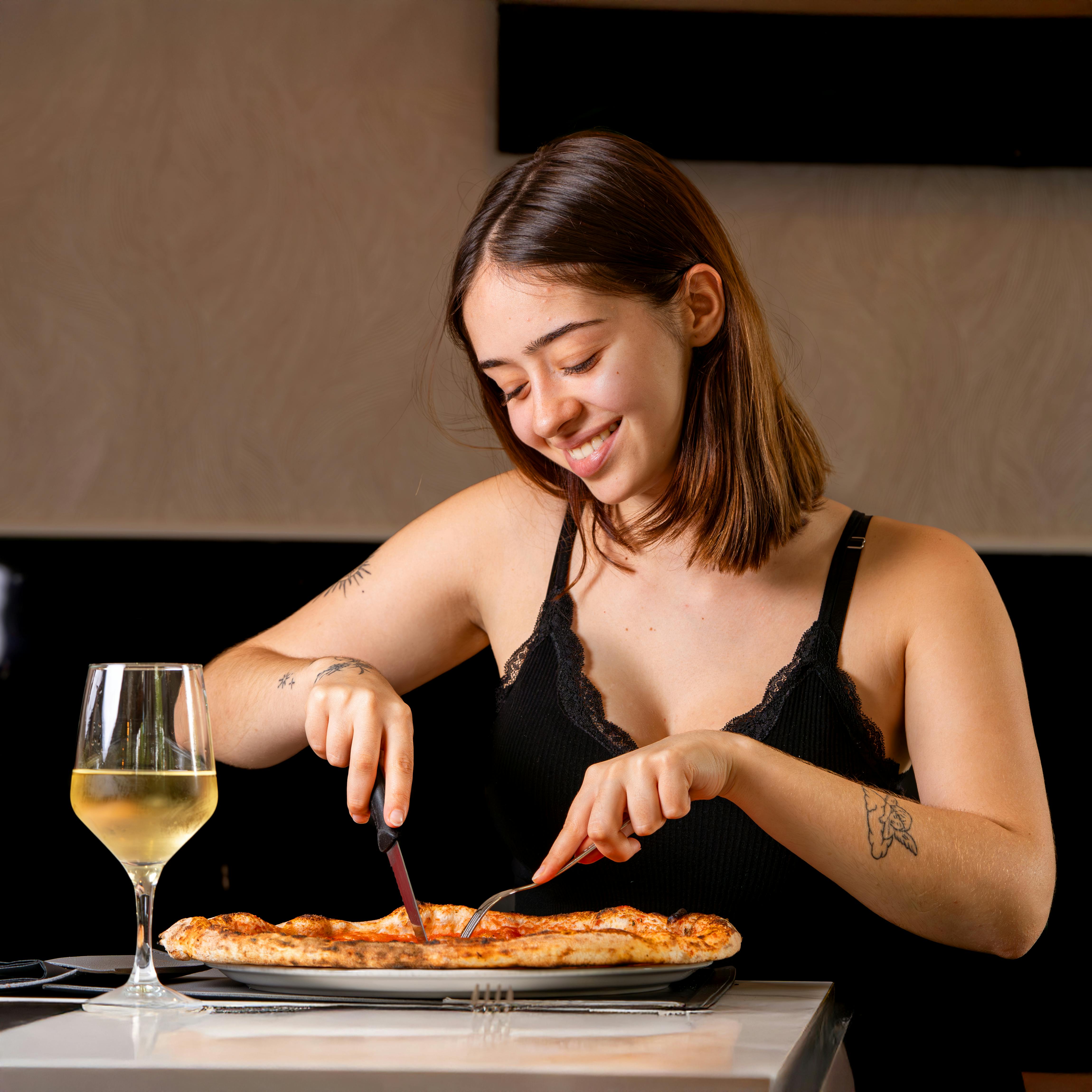 Smiling young woman cuts pizza in a cozy indoor setting with wine.
