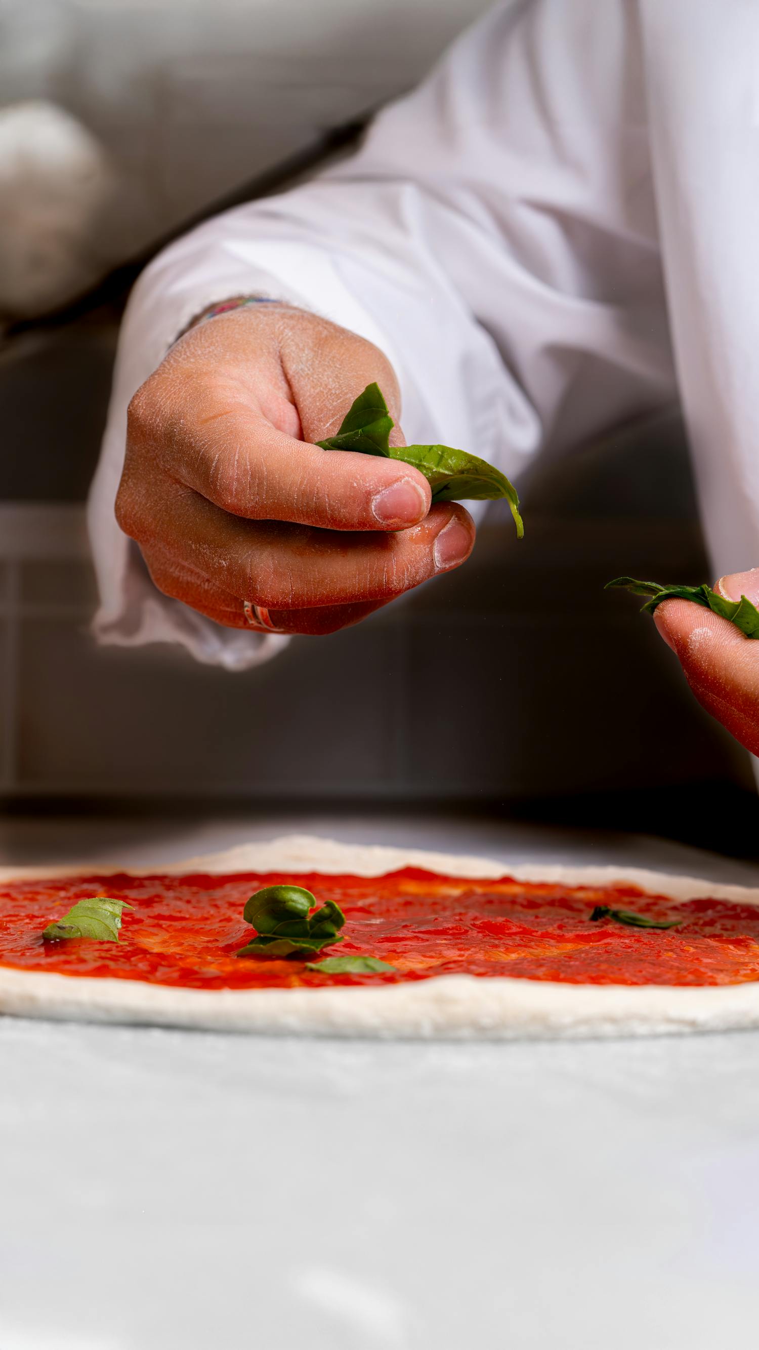 Hands adding basil on pizza dough with tomato sauce