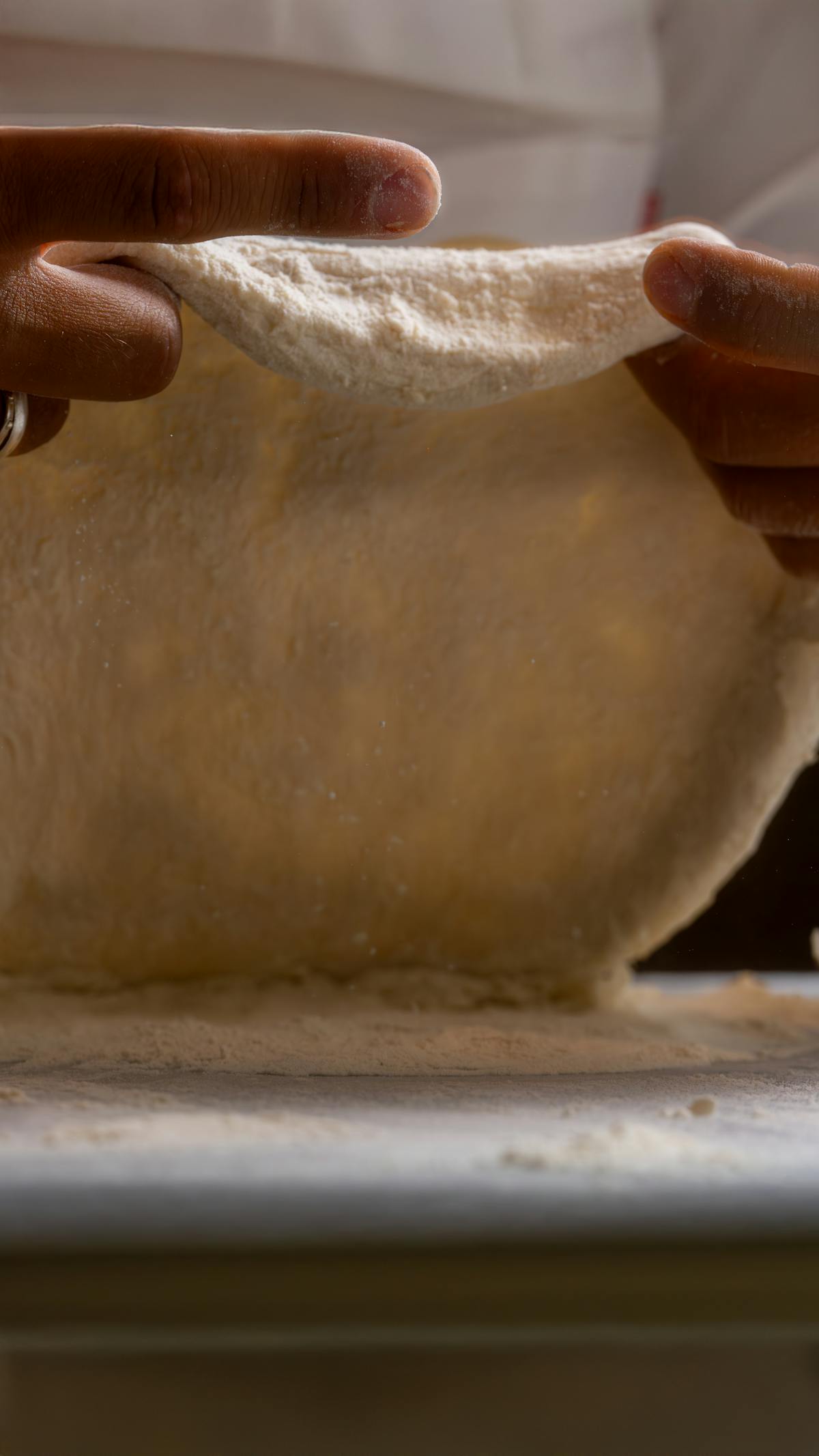 Primo piano di mani che allungano l’impasto per pizza