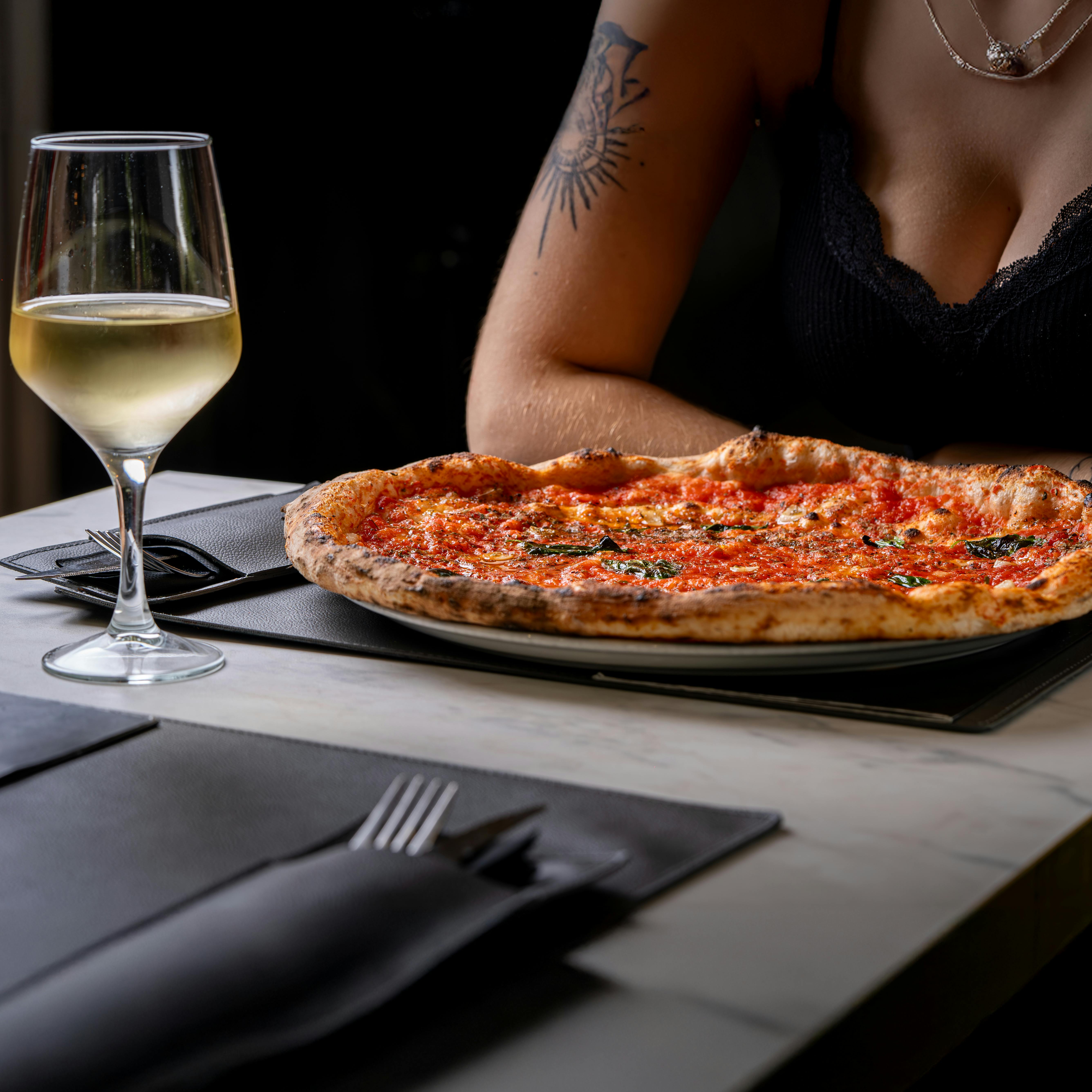 Delicious Italian pizza with a glass of white wine on a restaurant table setting.