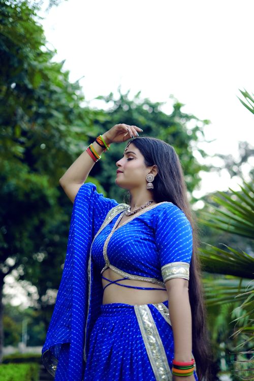Free Woman wearing a vibrant blue saree, posing elegantly in a lush outdoor setting. Stock Photo