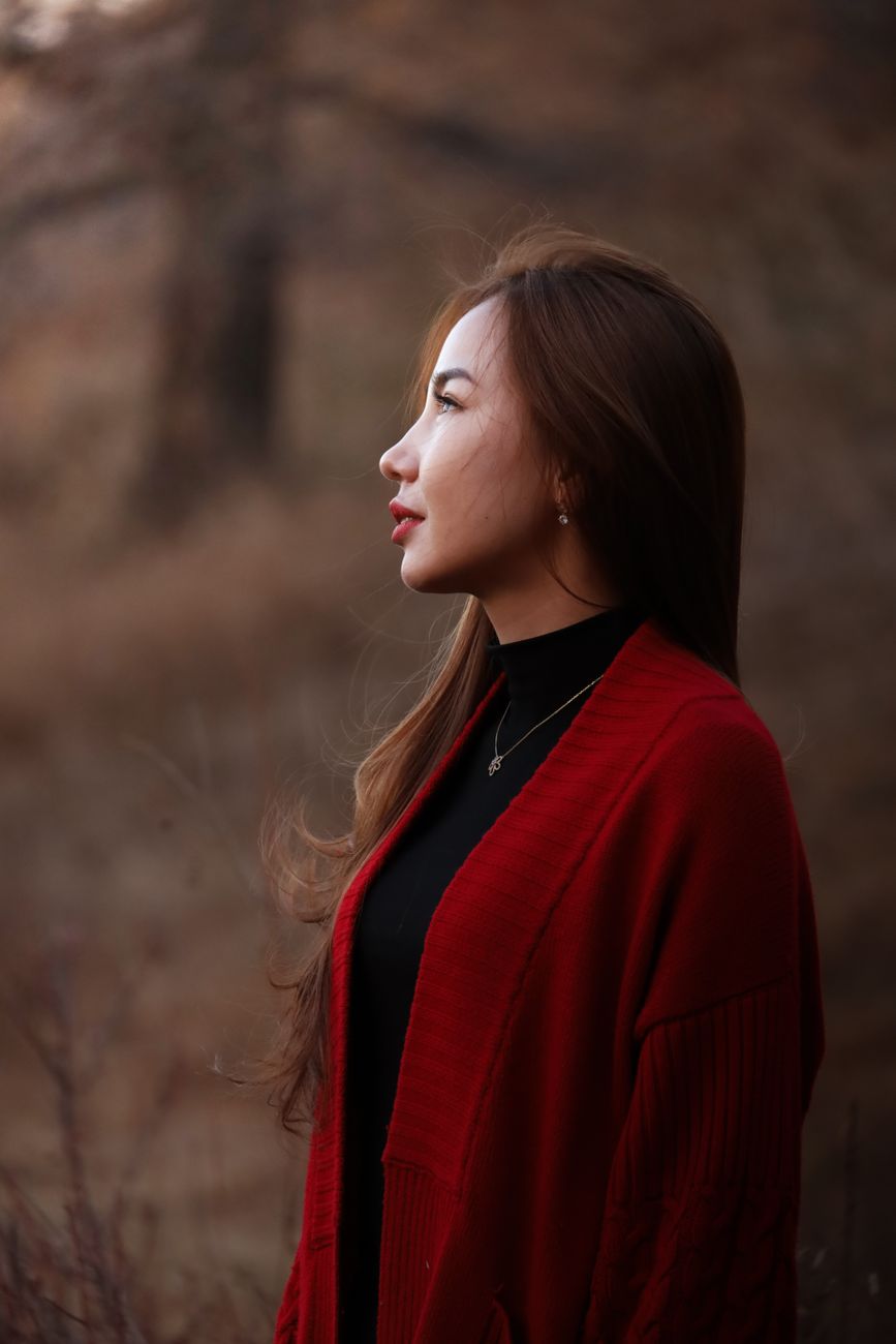 Profile of a woman in a red coat looking thoughtfully into the distance in a tranquil outdoor enviro