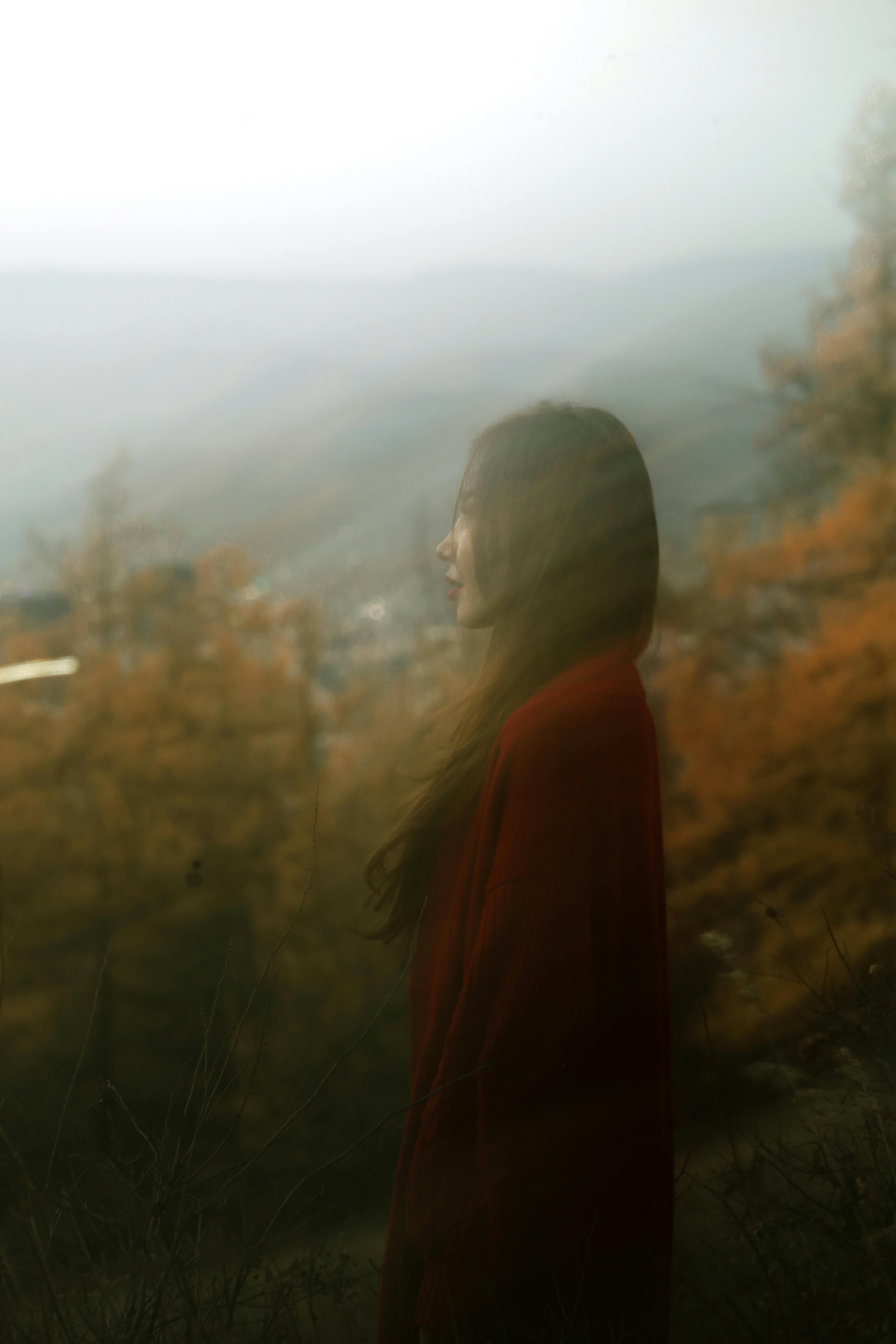 A woman in a red coat standing serenely in a misty autumn landscape.