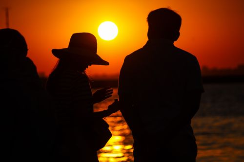 Free Two people enjoy a vibrant sunset by the water, creating a serene silhouette scene. Stock Photo