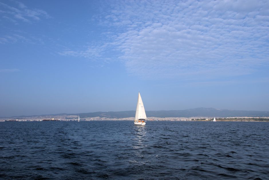 Best Mykonos Delos Rhenia Daily Cruise with BBQ, Drinks & Transfer Review 2026 - A serene view of a sailboat on the Aegean Sea near Thessaloniki, Greece under a clear blue sky.