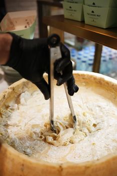 Pasta being tossed in a giant cheese wheel for a rich, creamy meal.
