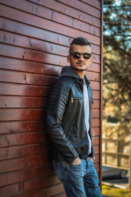 Free Stylish man in sunglasses leaning against a wooden wall outdoors. Stock Photo