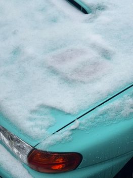 A snow-covered aqua car fender with visible taillight detail, suggesting winter.