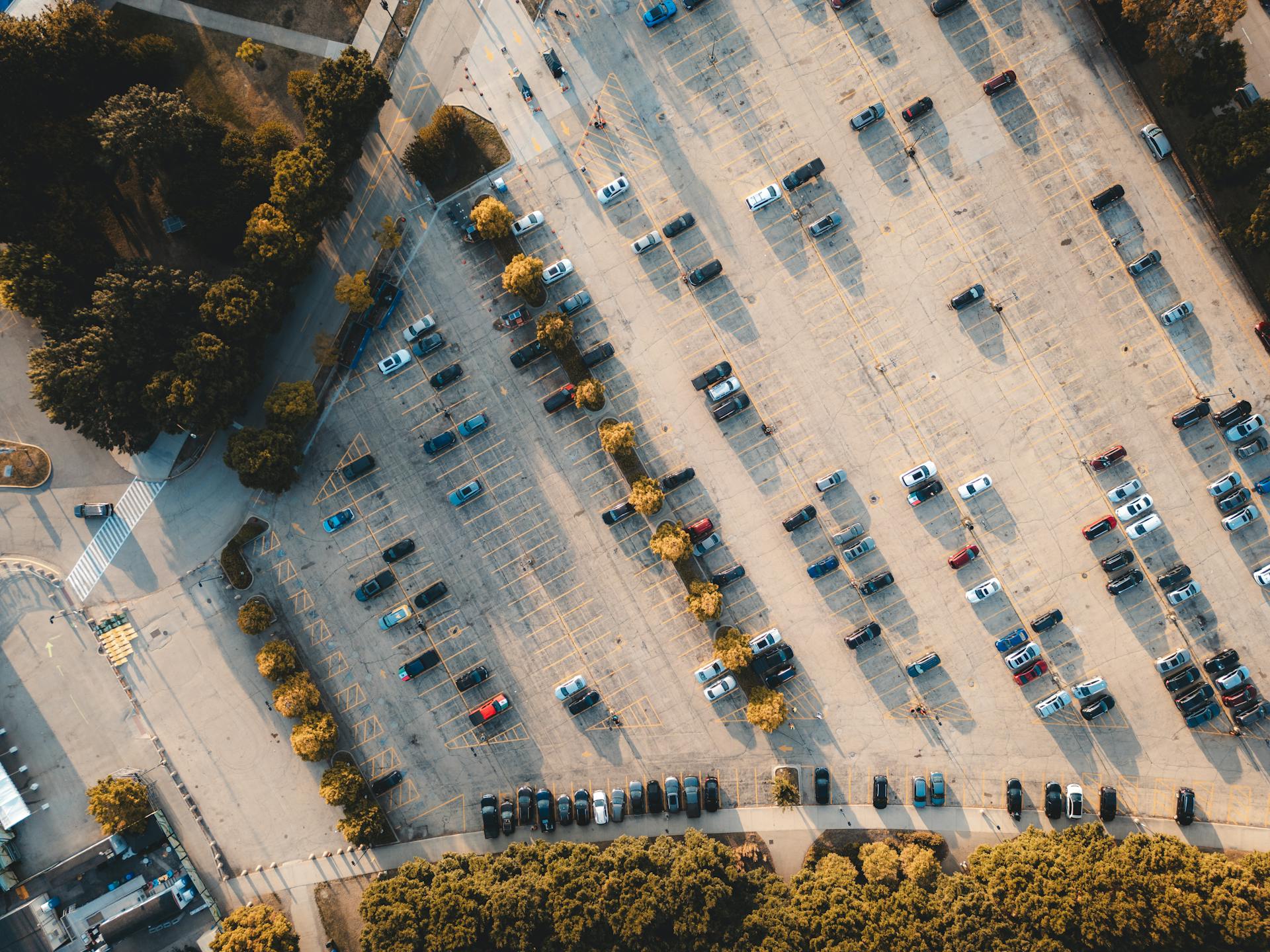 Top-down aerial shot of a parking lot with scattered cars and surrounding trees.