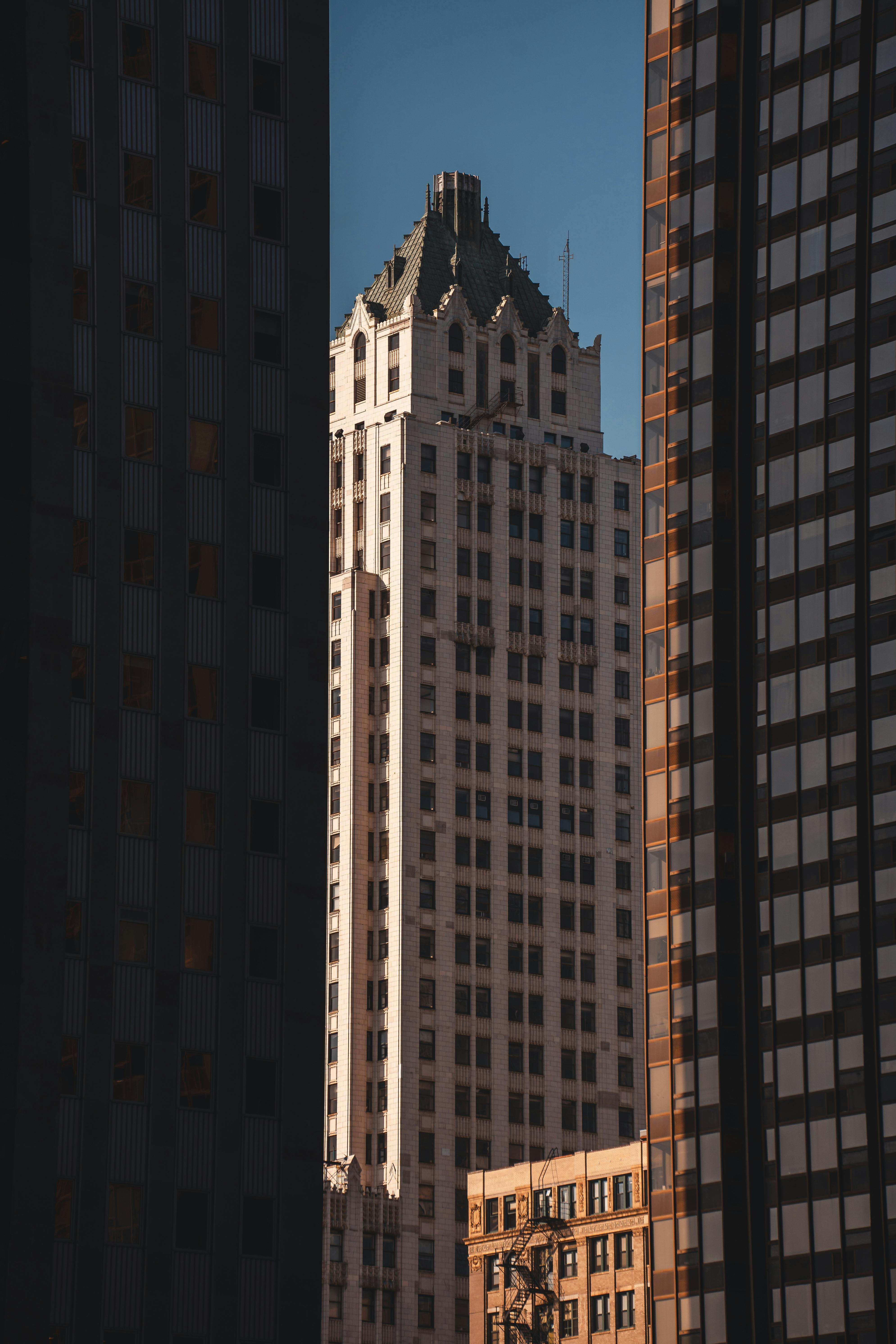 Tall iconic skyscraper framed by two modern buildings in a cityscape.