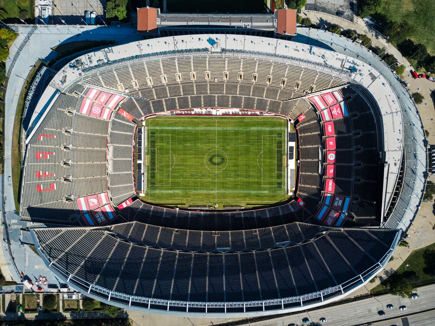 Top view of an empty soccer stadium with green field, showcasing seating arrangement under clear daylight.