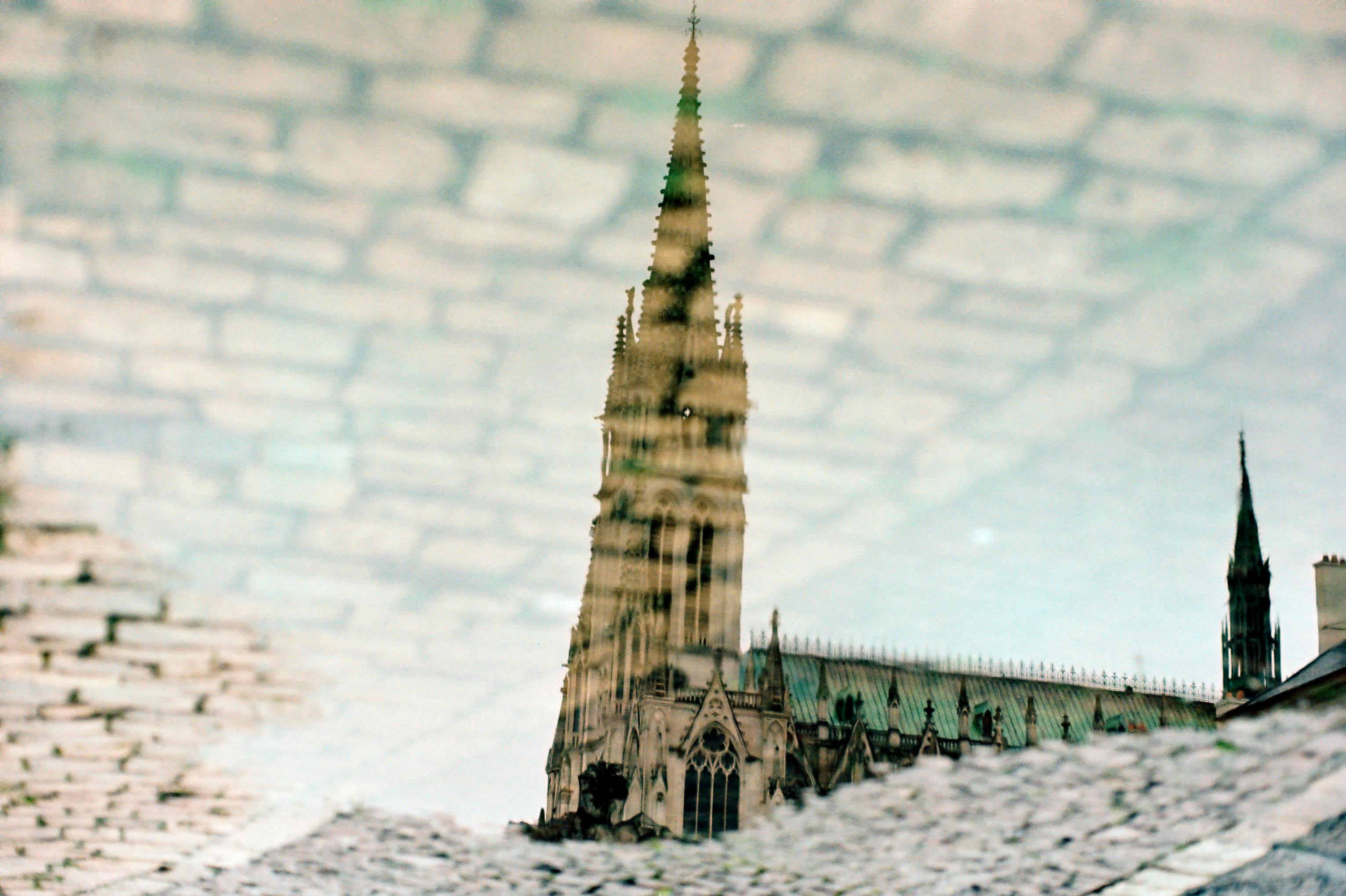 Reflection of a Gothic cathedral spire in a puddle on cobblestone pavement.