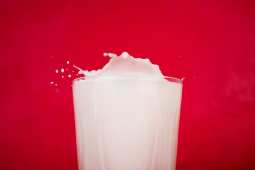 Free Dynamic milk splash in a glass with a vibrant red backdrop. Stock Photo