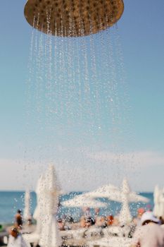 A refreshing shower on a sunlit beach with ocean view and beach umbrellas.