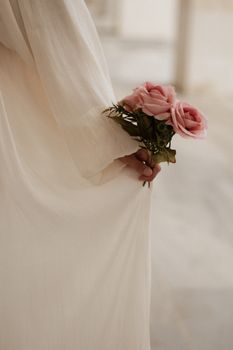 Graceful hand holding pink roses in a soft, elegant bridal gown.