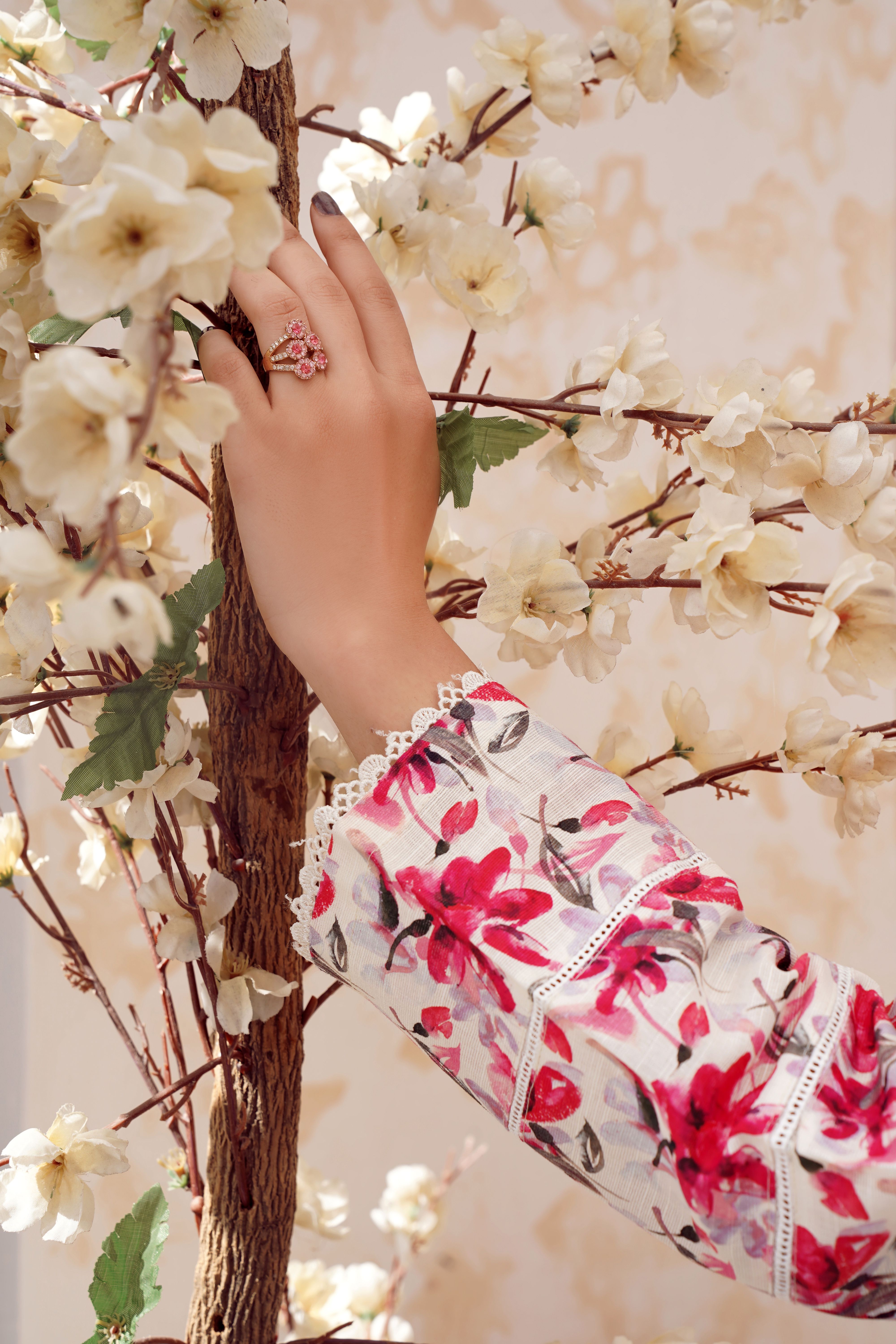 Close-up of a floral Pakistani dress and hand jewelry against a blossoming tree branch.
