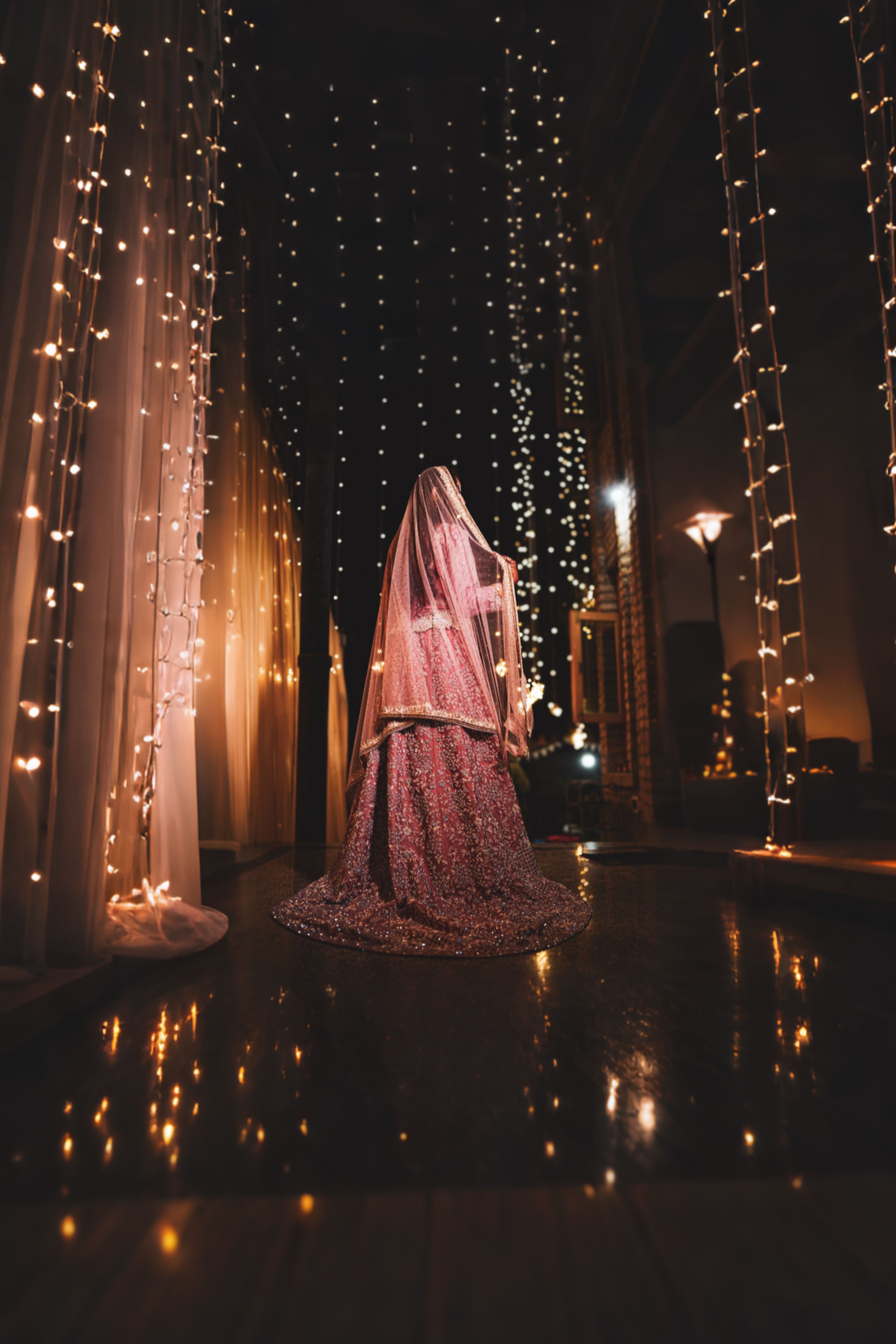 A bride in a traditional dress stands under twinkling lights, creating a magical atmosphere.