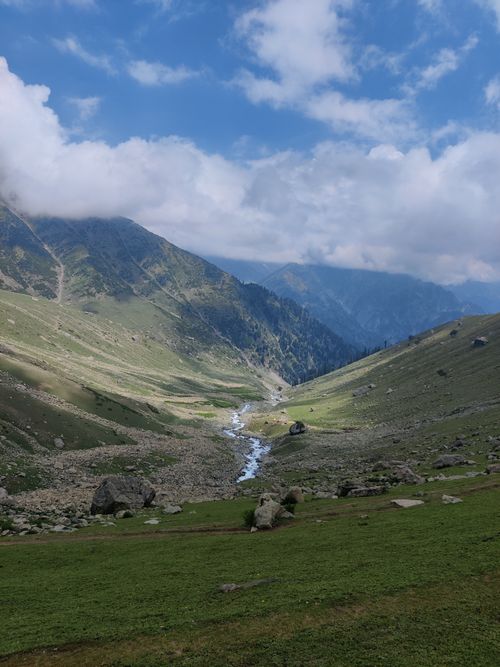Free A picturesque mountain valley scene with a flowing stream under a bright blue sky. Stock Photo