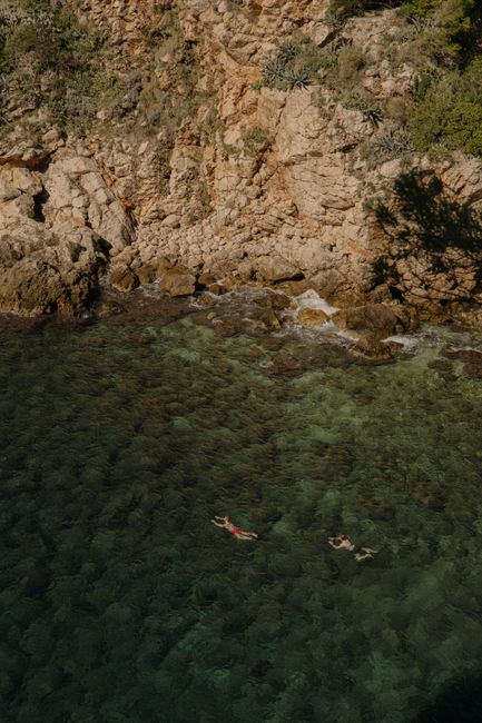 Aerial view of swimmers in clear waters near rocky cliffs in Croatia.