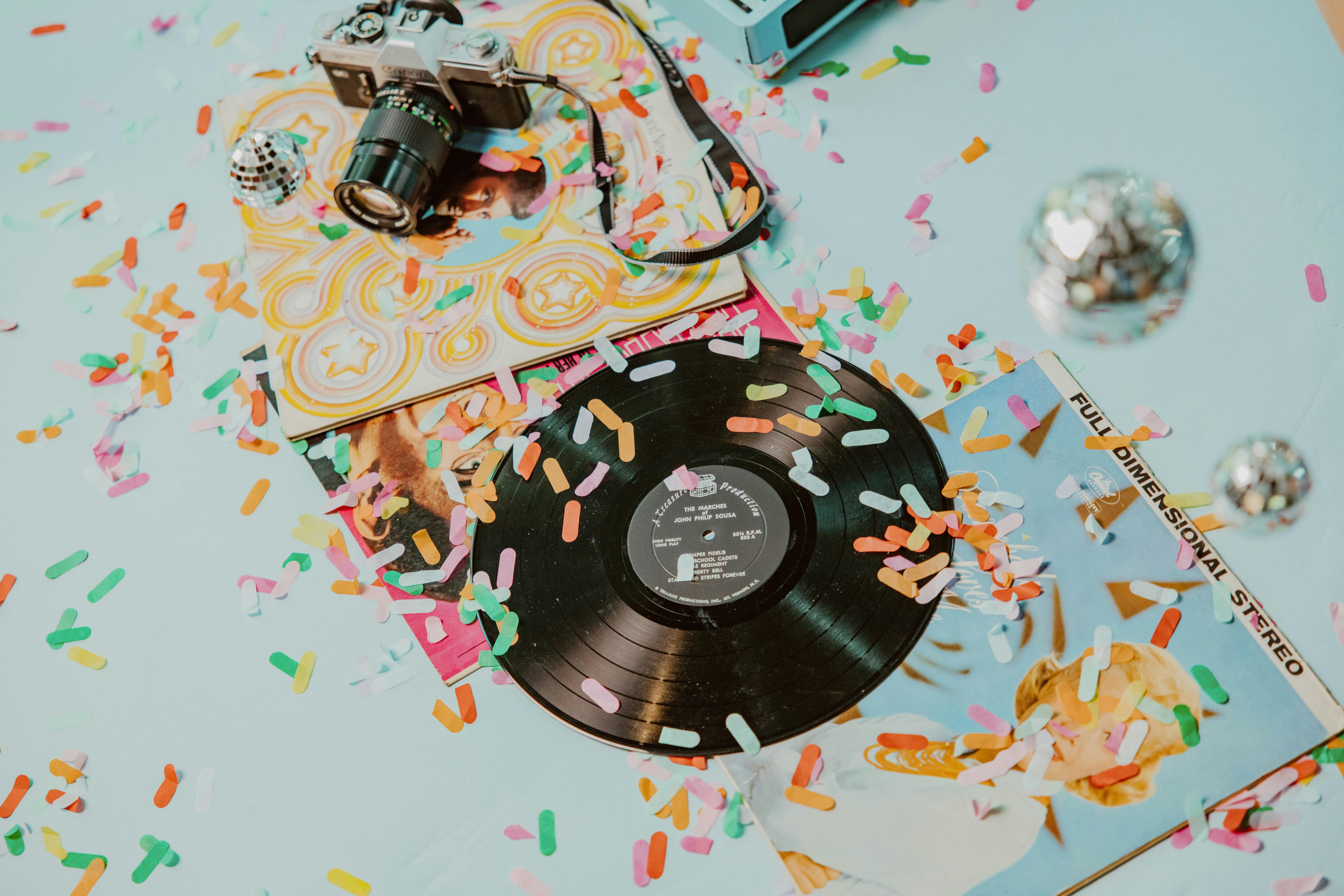 Colorful retro-themed composition with vinyl records and vintage camera adorned with confetti.