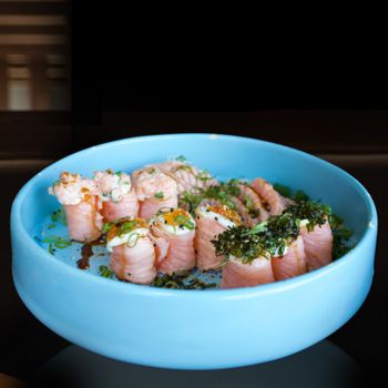 Freshly prepared salmon sushi rolls garnished with herbs in a blue bowl.
