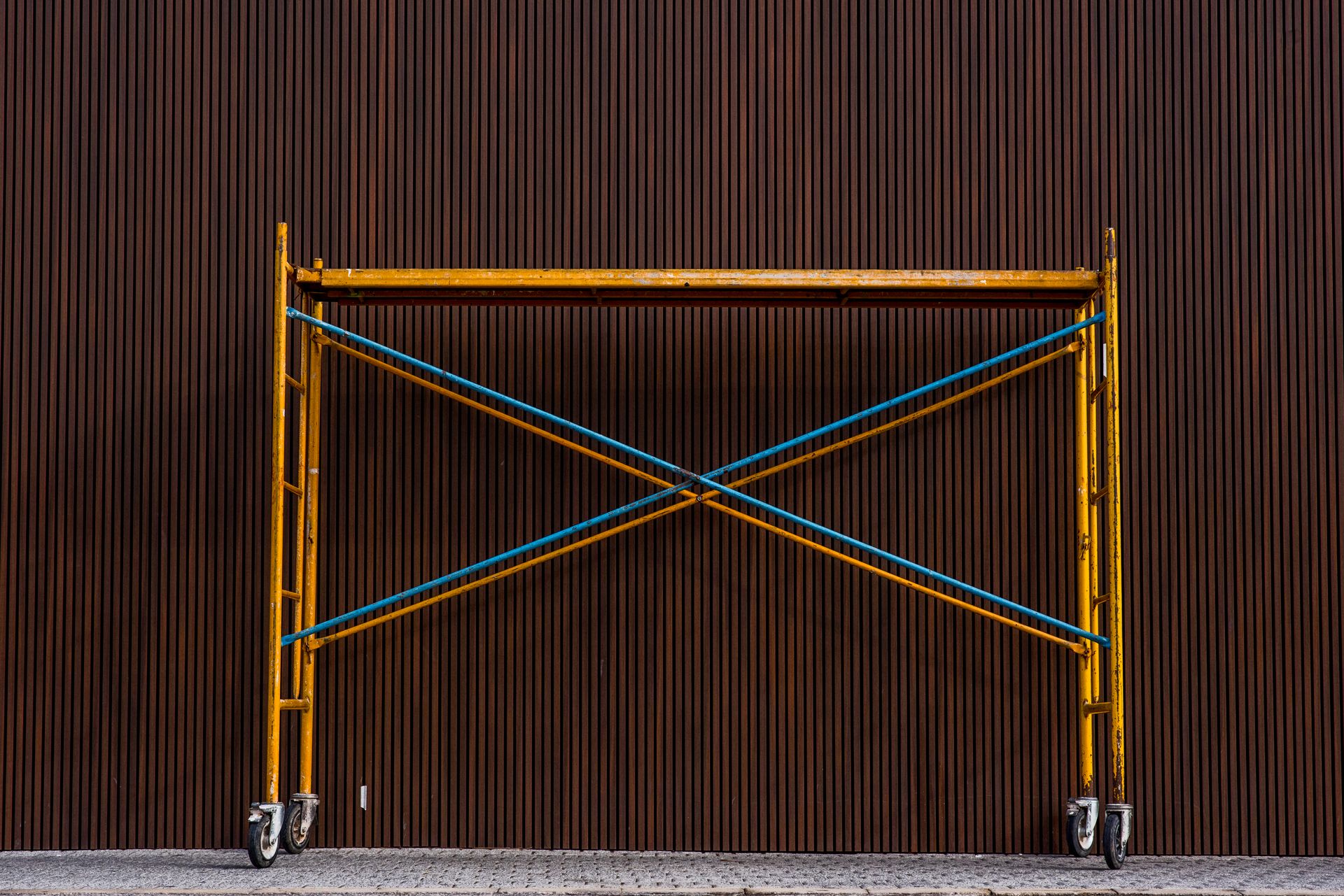 Yellow scaffolding setup against a corrugated brown wall. Perfect for construction and industrial themes.