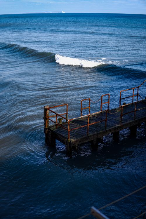 Free A weathered pier extends into the deep blue sea with gentle waves and a clear horizon. Stock Photo