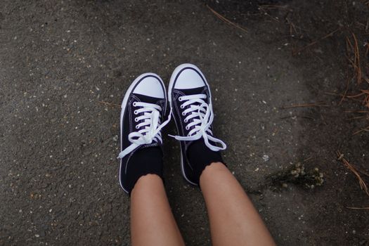 Black sneakers worn on pavement outdoors, showcasing casual style footwear.