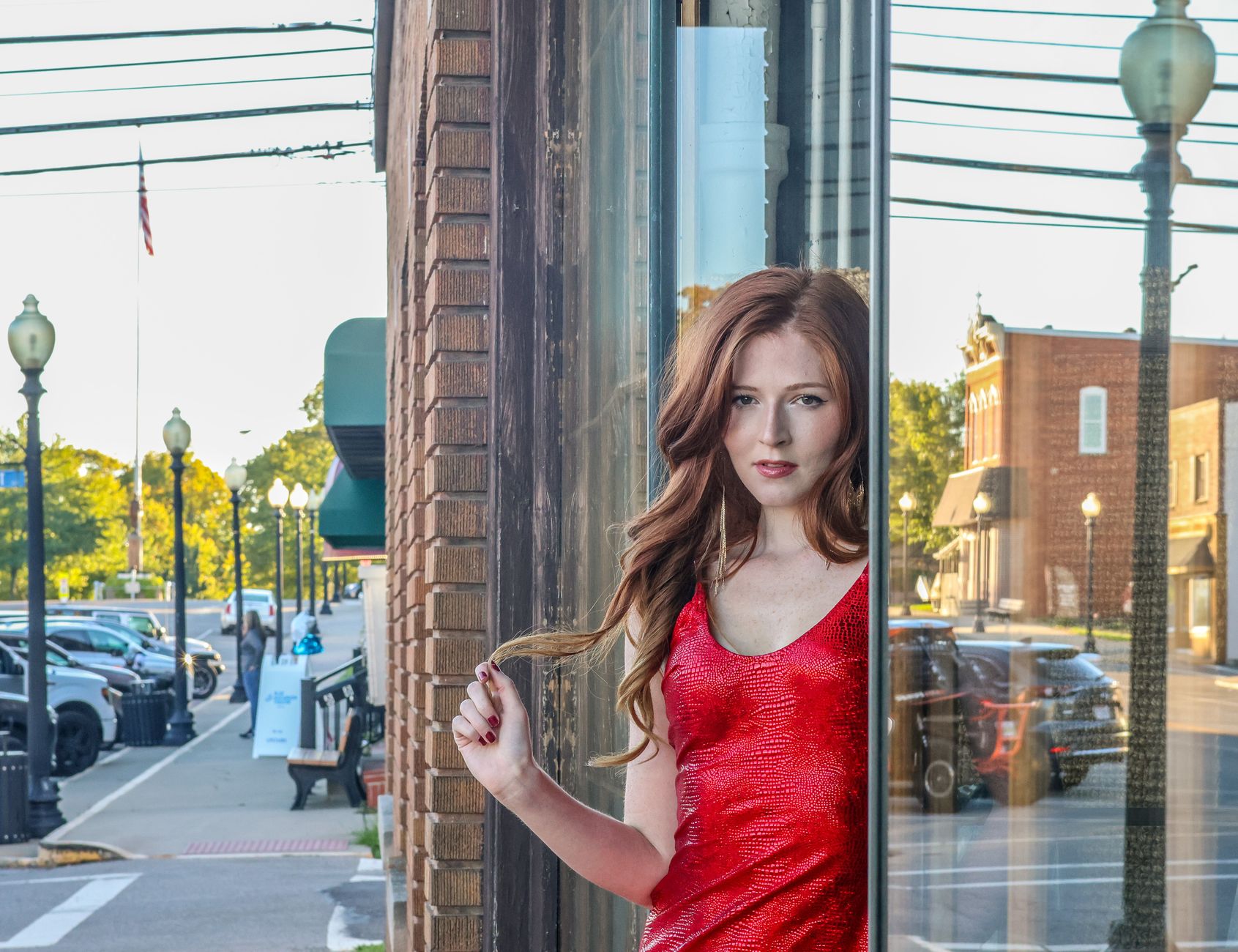 Elegant woman in red dress gazes through window in a small town setting.