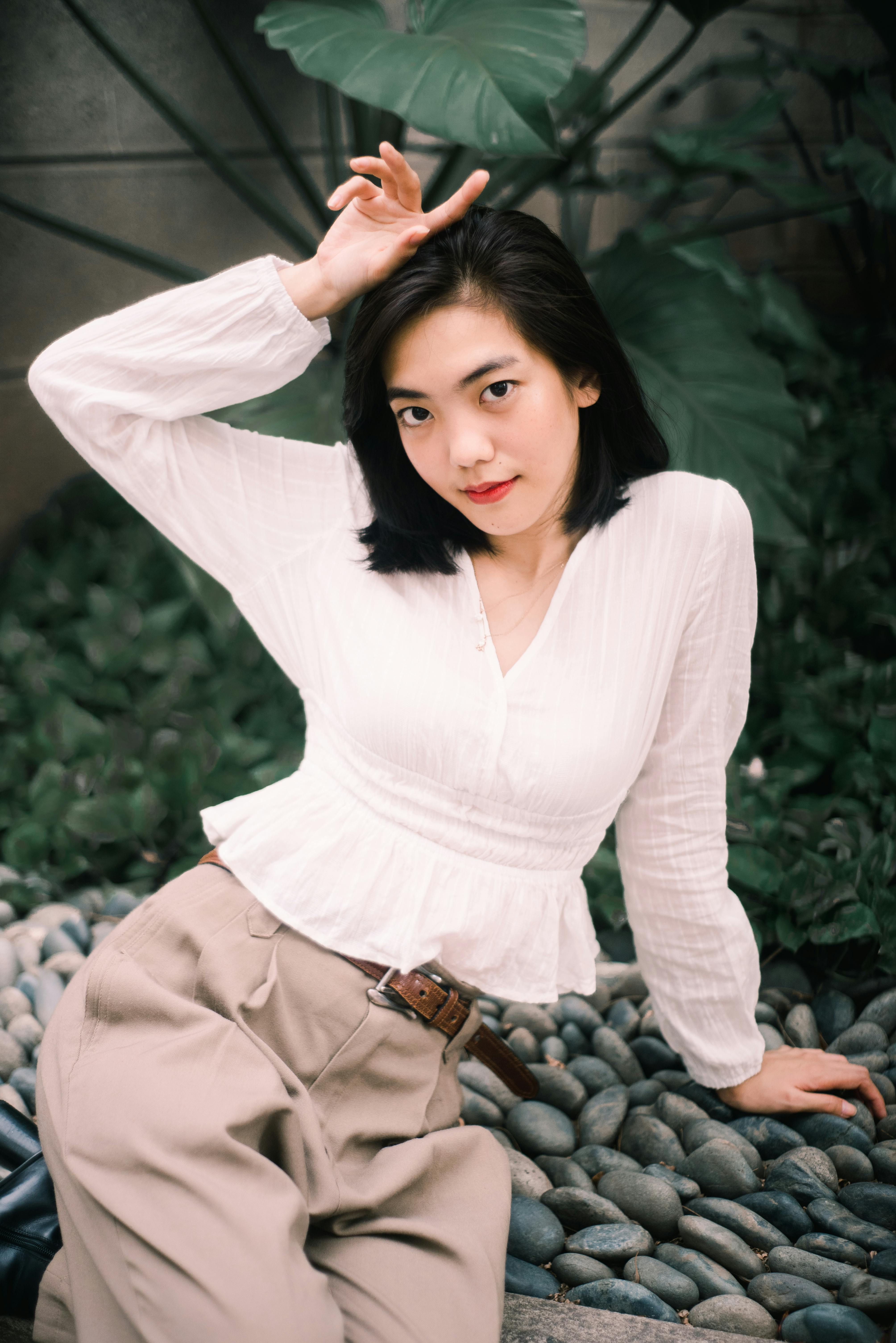 一位穿着白色衬衫和米色裤子的时尚女性在户外鹅卵石上摆着姿势