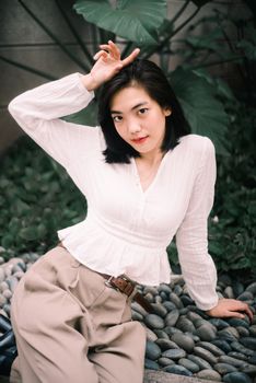 一位穿着白色衬衫和米色裤子的时尚女性在户外鹅卵石上摆着姿势
