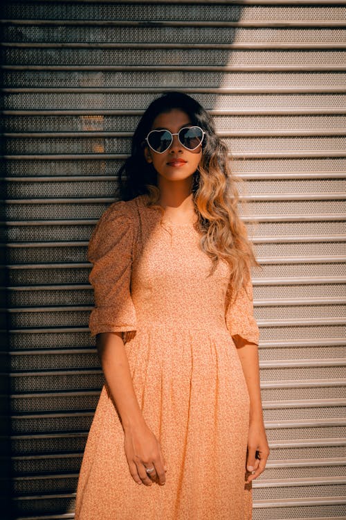 Woman Wearing an Orange Dress and Heart shaped Glasses Leaning on Wall