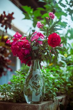 A beautiful bouquet of red blooms in a decorative glass vase amidst lush garden greenery.