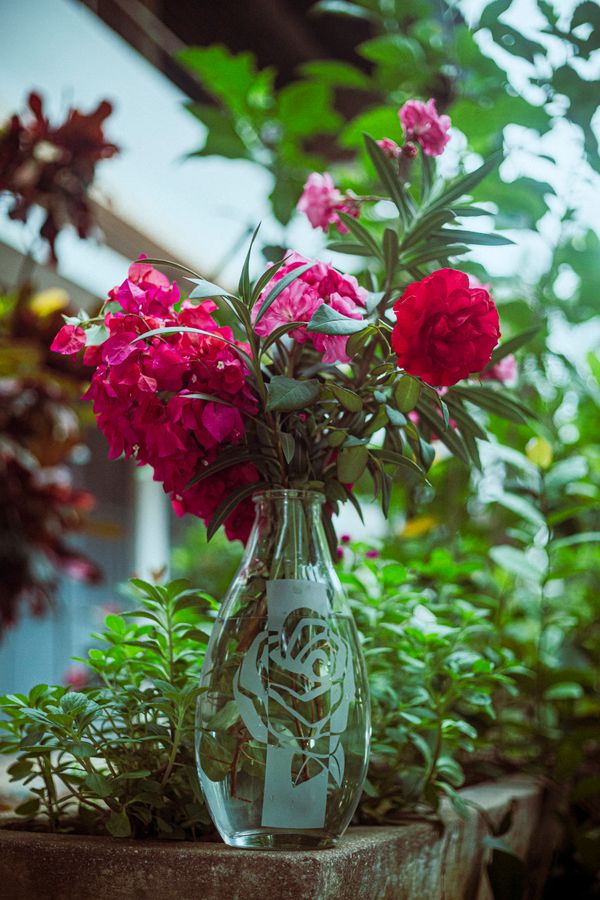 Um belo buquê de flores vermelhas em um vaso de vidro decorativo, rodeado por uma vegetação exuberante no jardim.