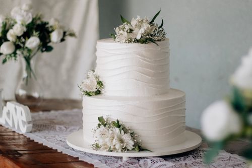 Free Beautiful two-tier white wedding cake adorned with fresh flowers on a rustic wooden table. Stock Photo