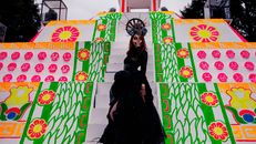 A woman dressed as a Catrina poses on colorful Day of the Dead themed steps.