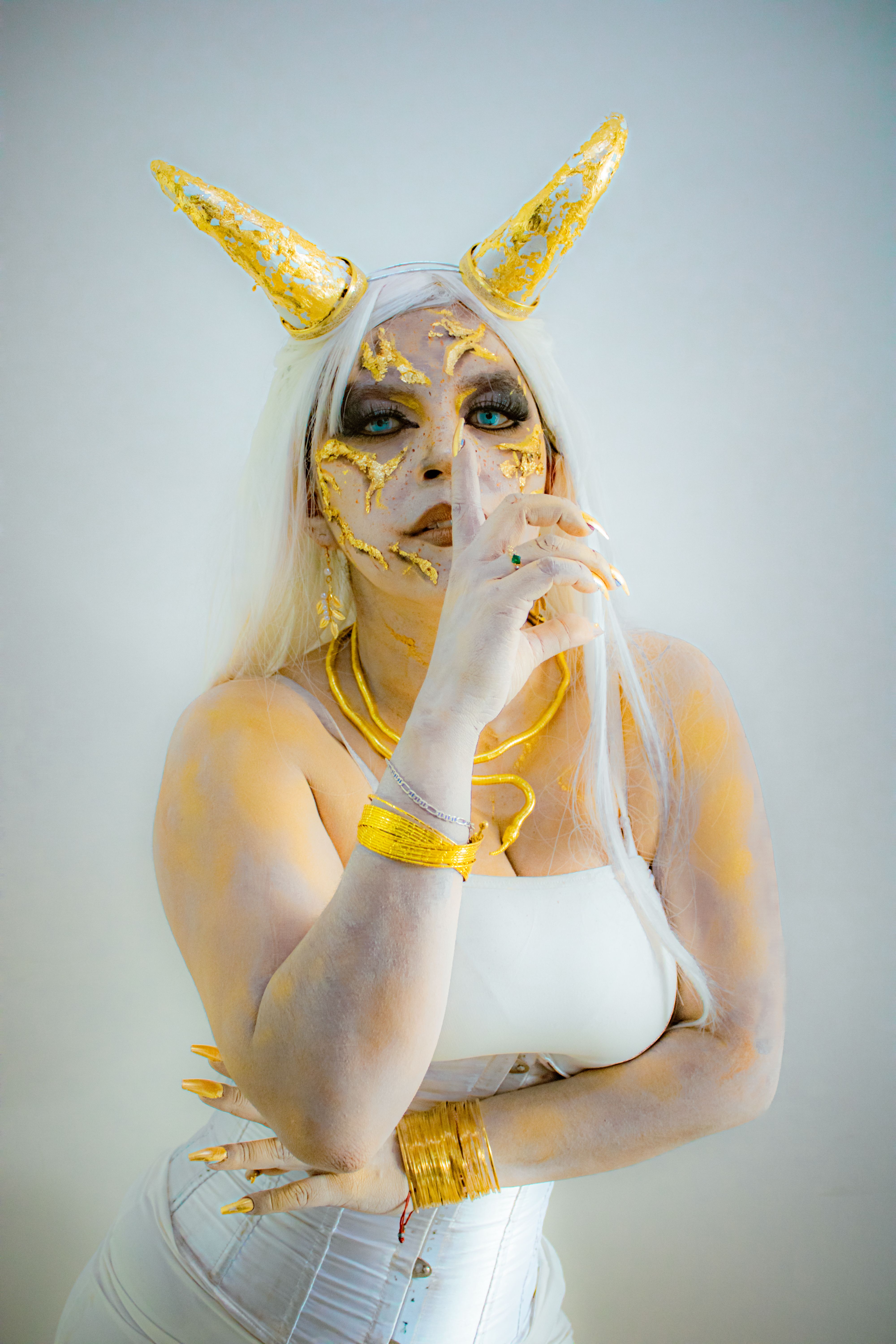 A woman in artistic horror makeup with gold horns in a creative costume pose.