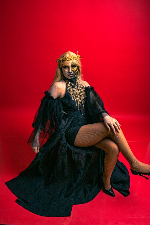 Free A woman in a dramatic horror costume with gold makeup sits against a red backdrop. Stock Photo