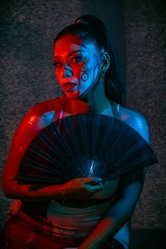 A woman with artistic makeup in red and blue light, holding a fan in Mexico City.