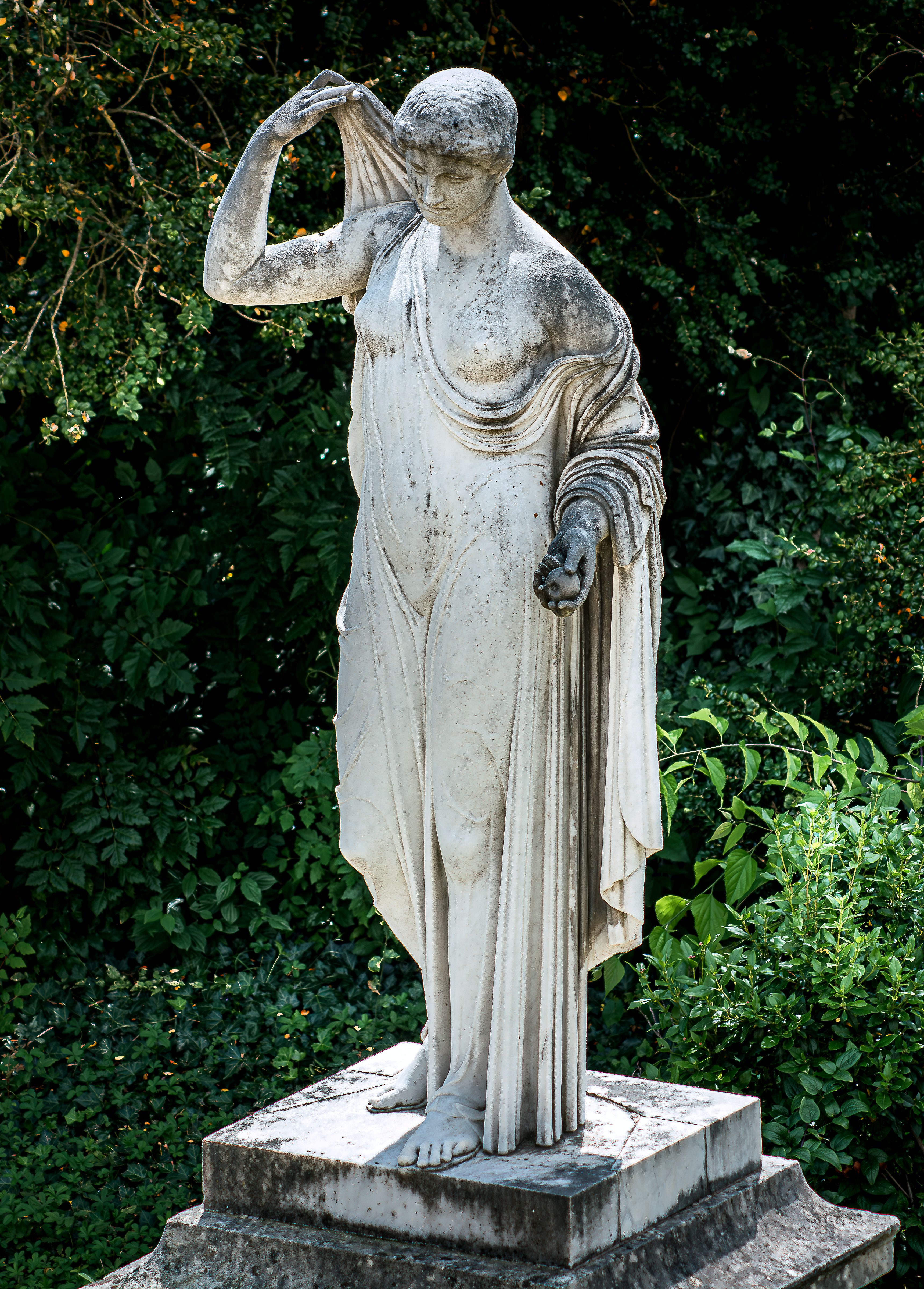 Elegant marble statue of a draped woman in a lush garden background.